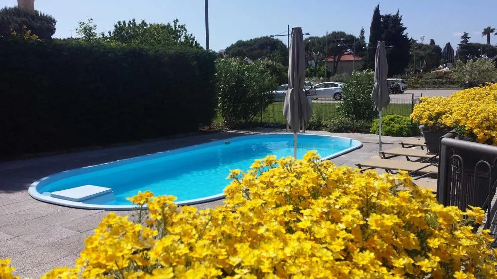 Piscina ovale circondata da siepi e fiori gialli con ombrelloni chiusi e lettini