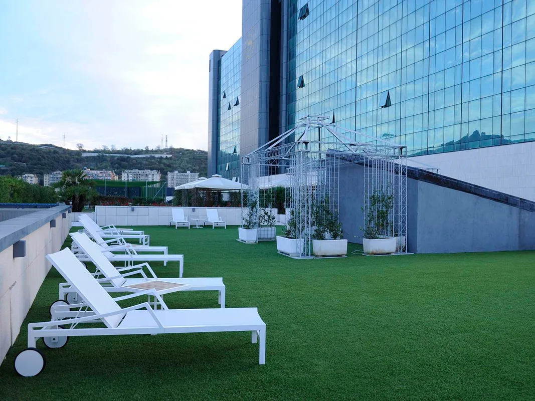 Terrazza con prato sintetico e lettini bianchi davanti alla facciata in vetro dell'hotel