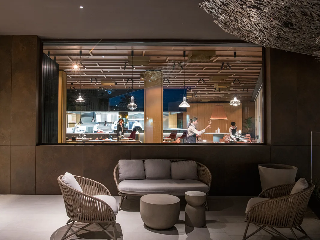 Lounge moderna con poltrone in vimini e cucina a vista del ristorante illuminata di sera