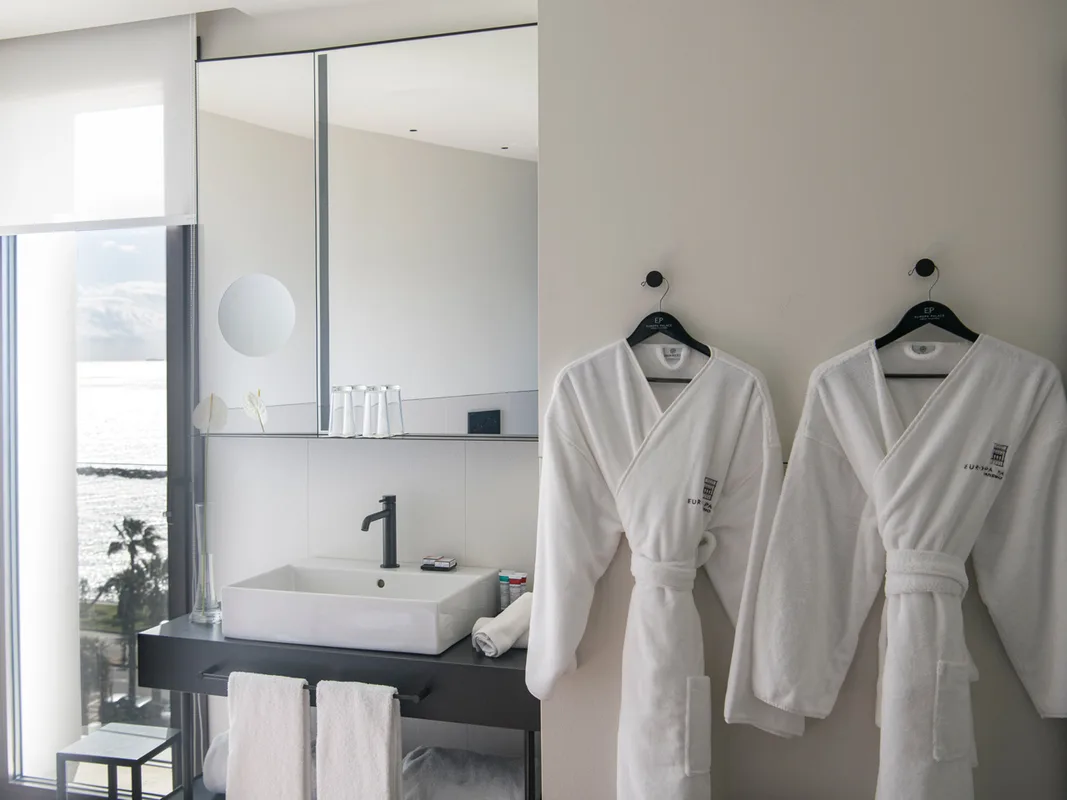 Bagno elegante con lavabo, specchio e accappatoi bianchi con vista sul mare