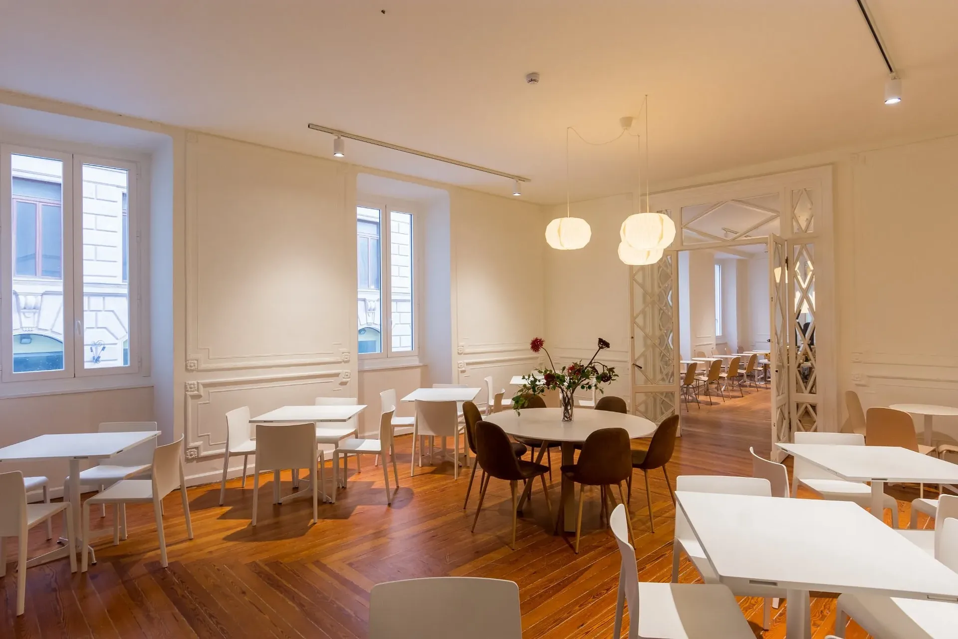 Ampia sala ristorante con pavimento in legno, pareti decorate e tavoli bianchi