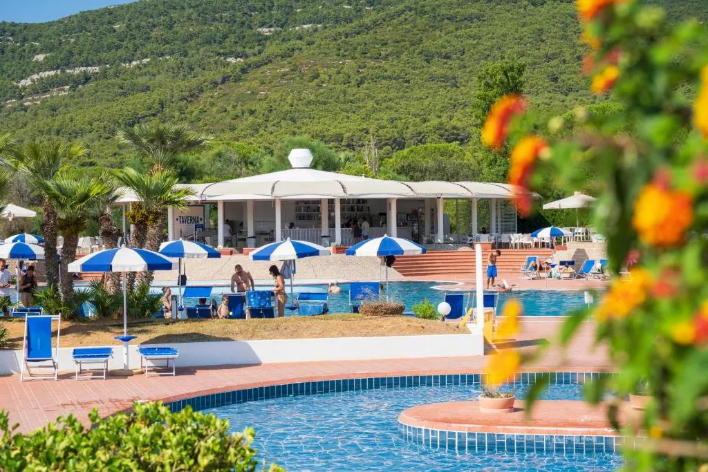 Area piscina con ombrelloni blu, bagnanti e bar Taverna immerso nel verde