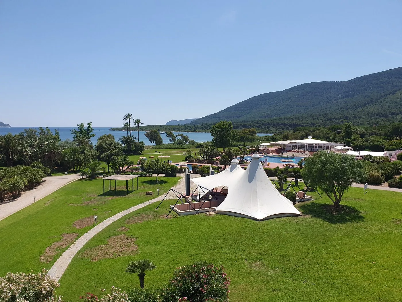 Giardino del resort con tenda bianca, prato verde e vista sul mare e le colline