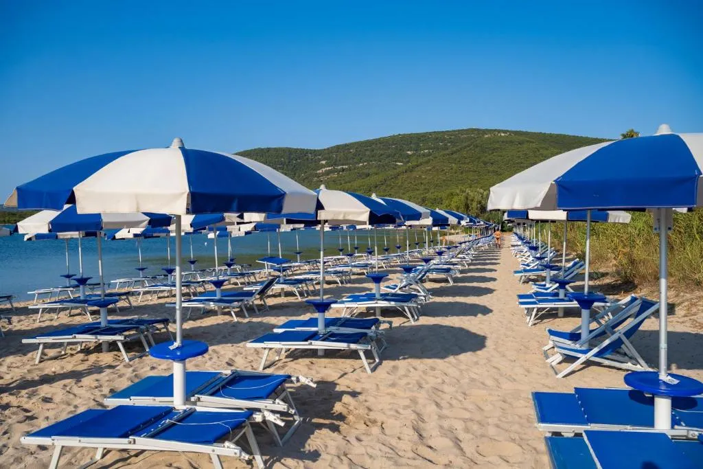 Spiaggia con file di lettini e ombrelloni blu e bianchi e collina verde