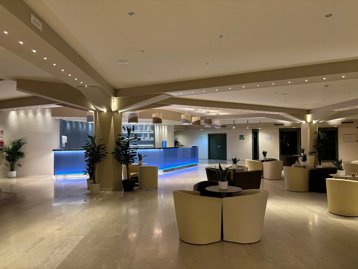 Hall del resort con reception illuminata di blu, poltrone e piante