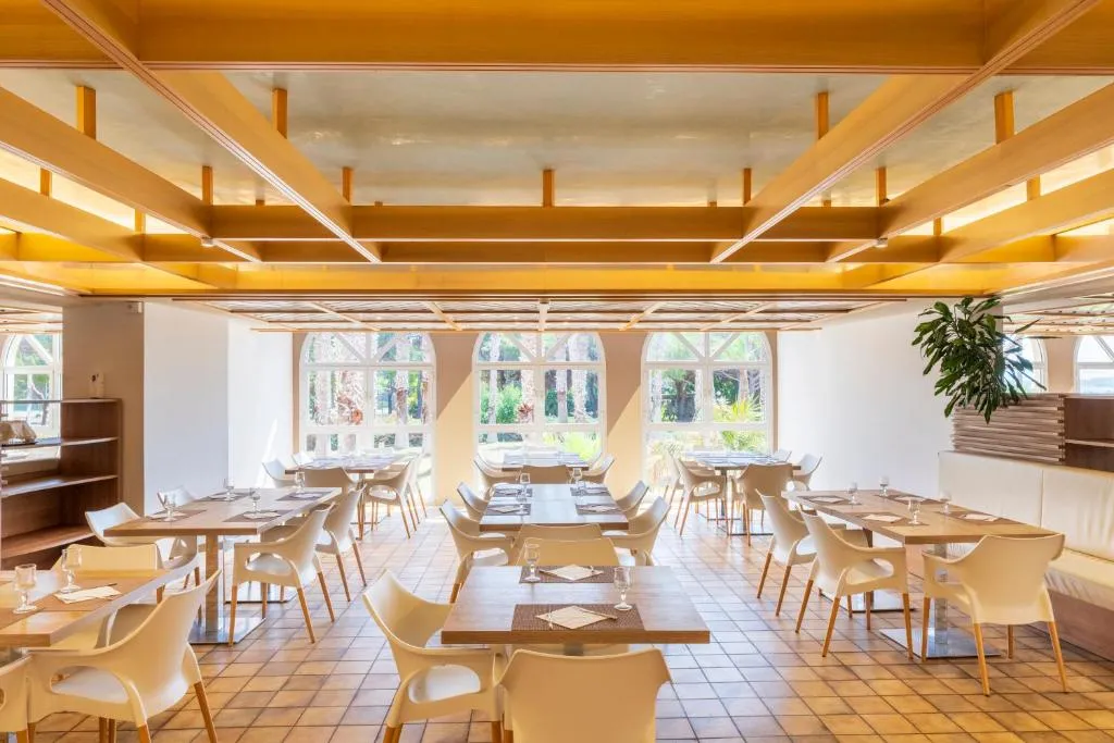Sala ristorante luminosa con tavoli in legno, sedie bianche e grandi finestre
