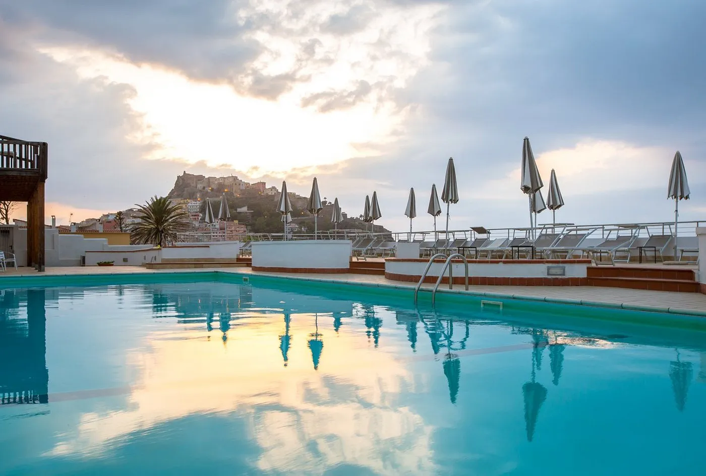 Piscina al tramonto con ombrelloni chiusi e borgo di Castelsardo sullo sfondo