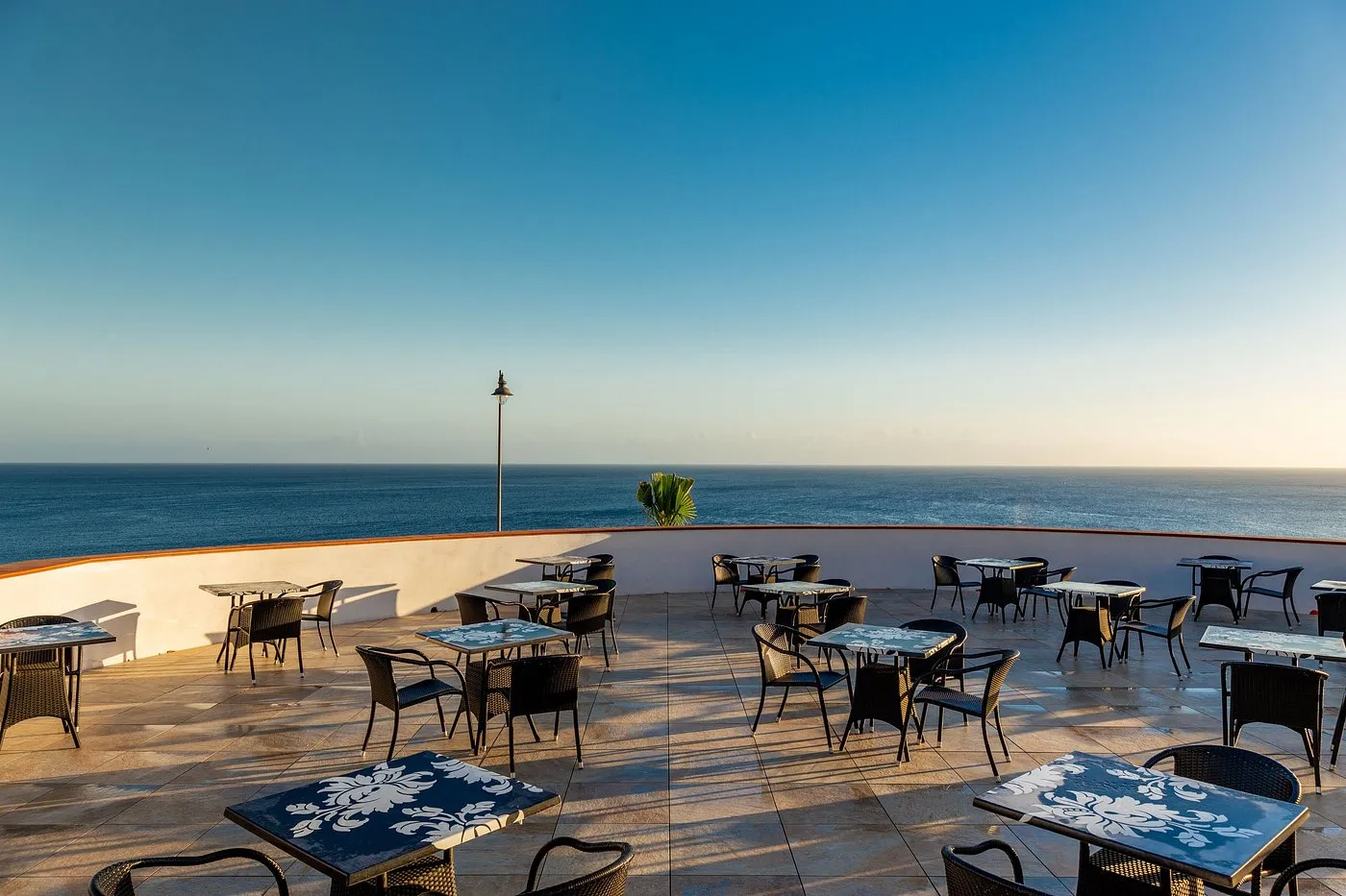 Terrazza ristorante con tavoli e sedie affacciata direttamente sul mare al tramonto