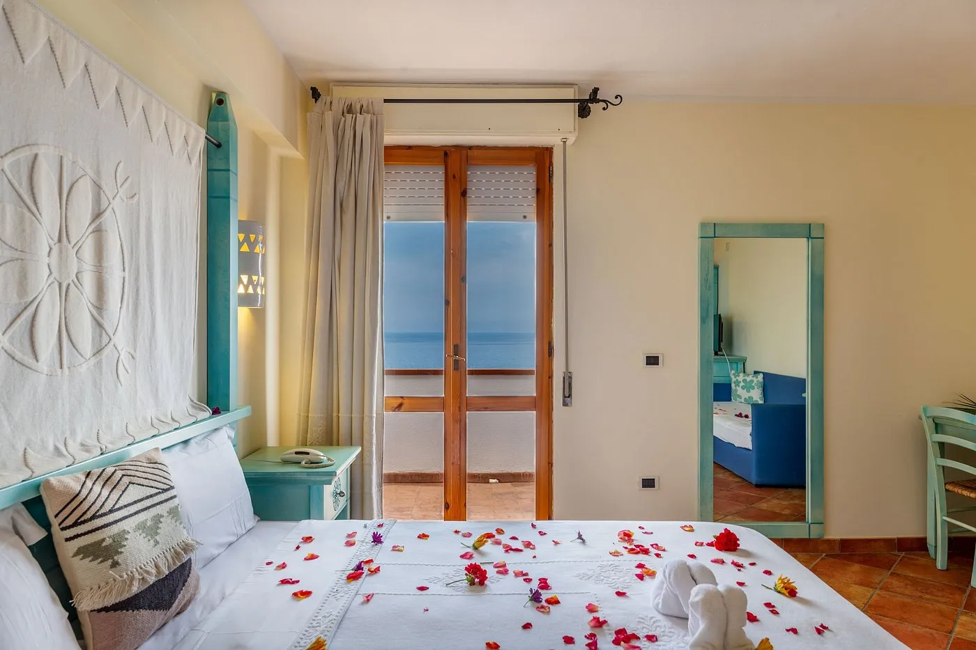 Camera romantica con petali sul letto e porta finestra con vista mare