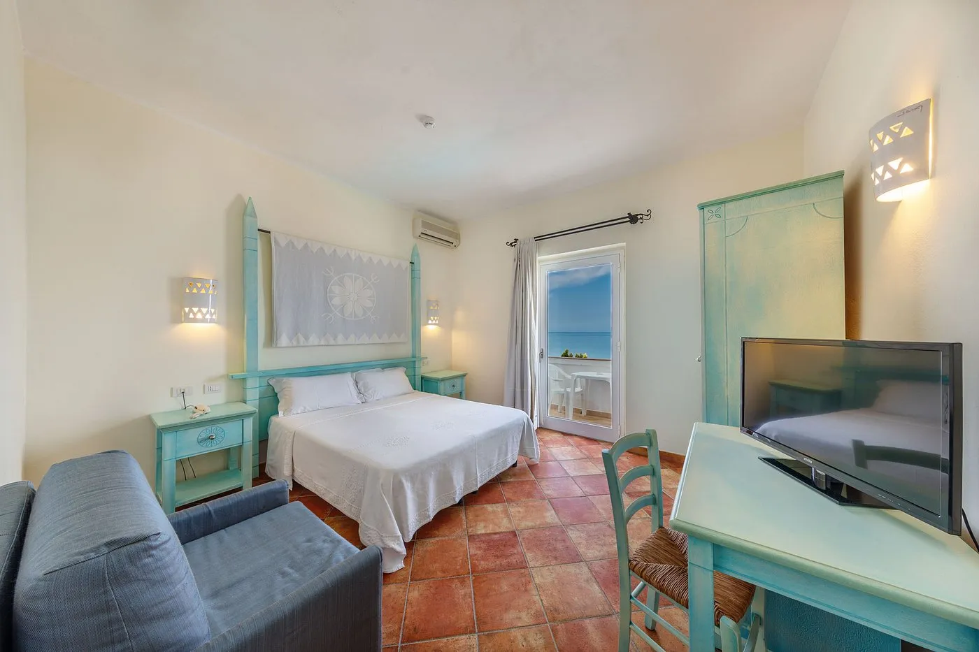 Camera matrimoniale con arredi azzurri, TV e balcone con vista mare