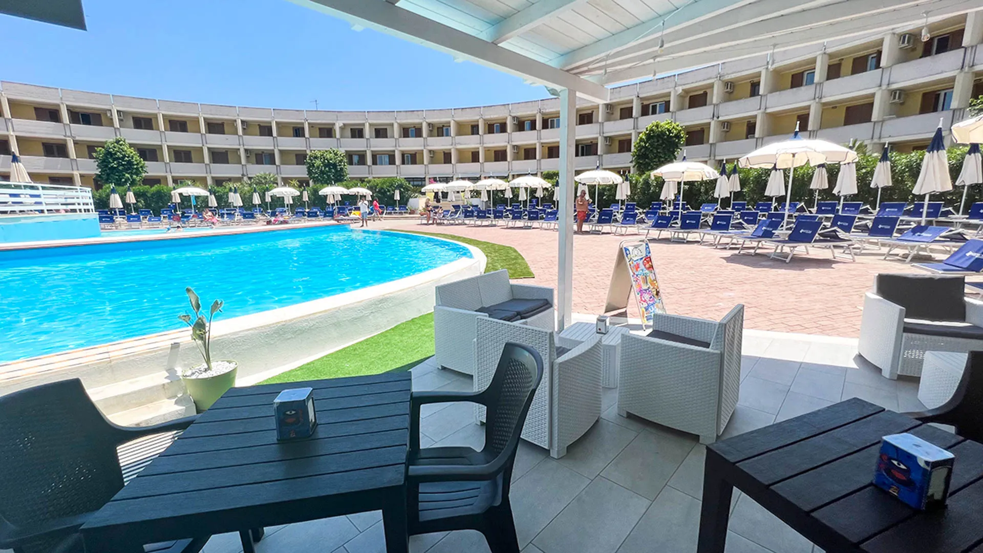 Area lounge coperta con divani in rattan bianco affacciata sulla piscina