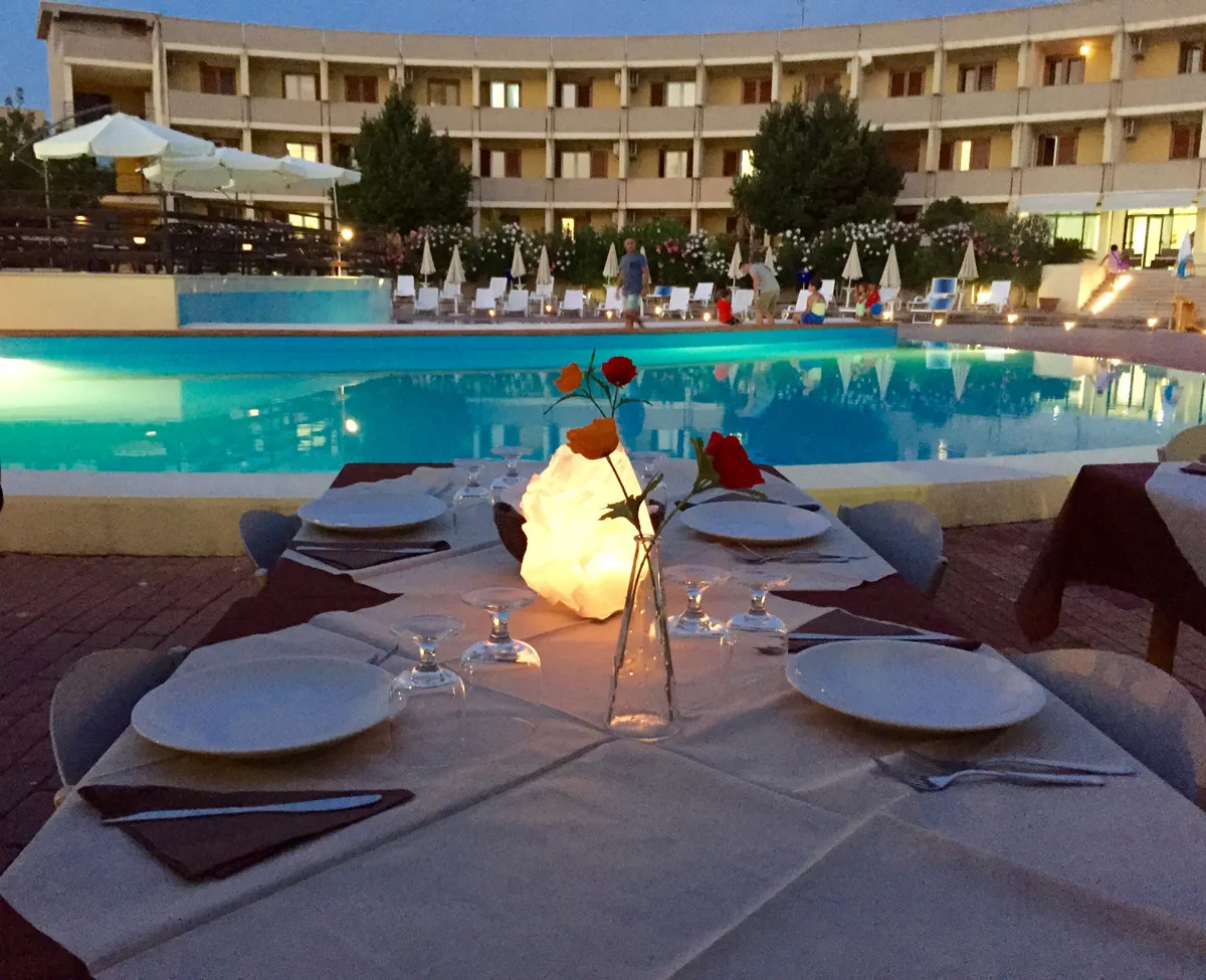 Tavolo apparecchiato per cena romantica al tramonto a bordo piscina con rose