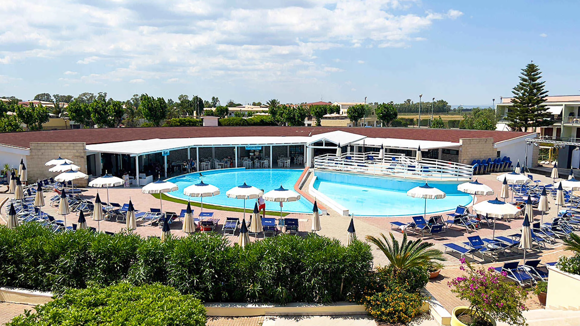 Vista dall'alto della piscina con bar e ristorante, lettini blu e ombrelloni