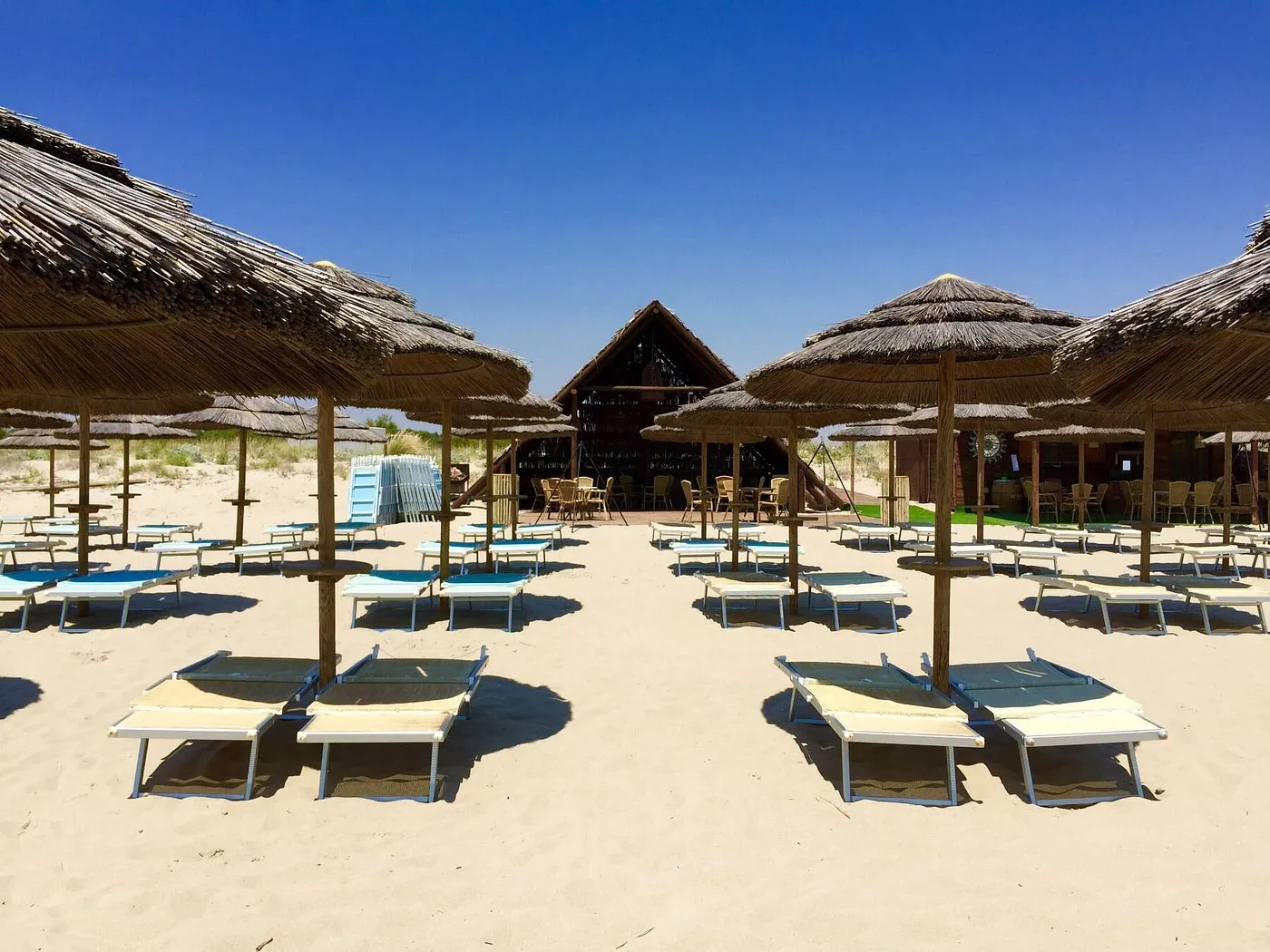 Lettini e ombrelloni in paglia sulla spiaggia con struttura in legno sullo sfondo