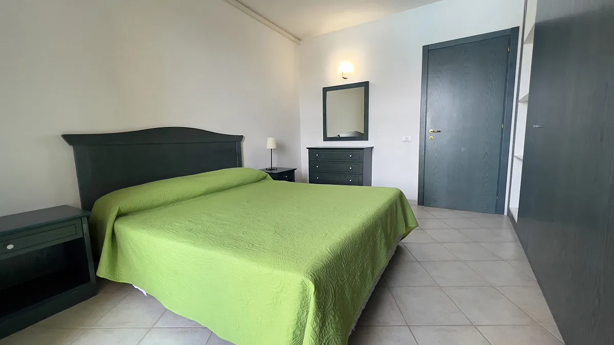 Camera da letto matrimoniale con copriletto verde e arredi scuri