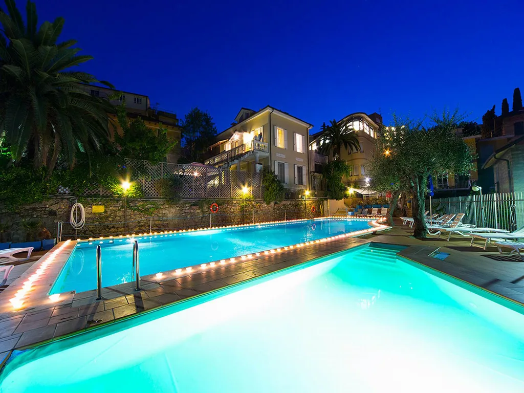 Piscina illuminata di sera con luci soffuse e l'hotel sullo sfondo al crepuscolo