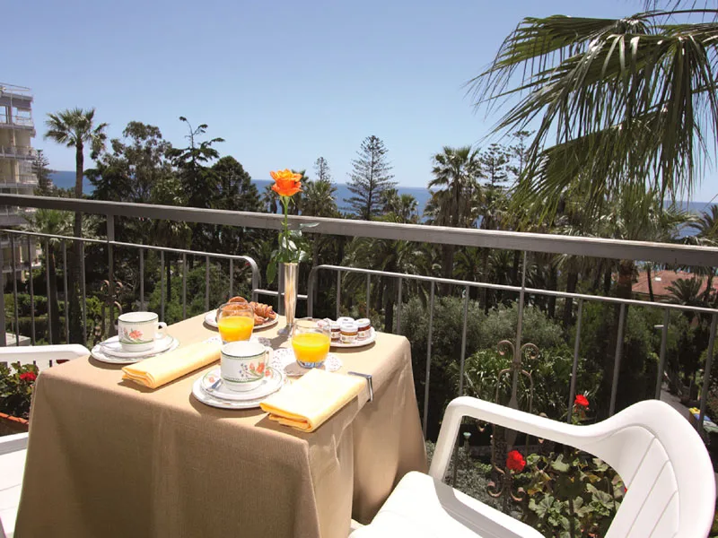 Colazione servita sul balcone con vista su giardino di palme e mare