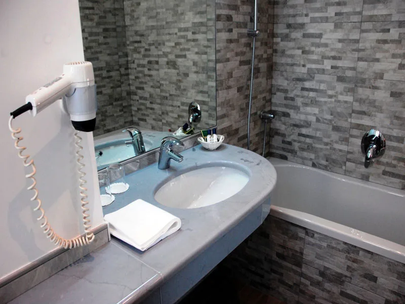 Bagno con lavabo in marmo, asciugacapelli, specchio e vasca