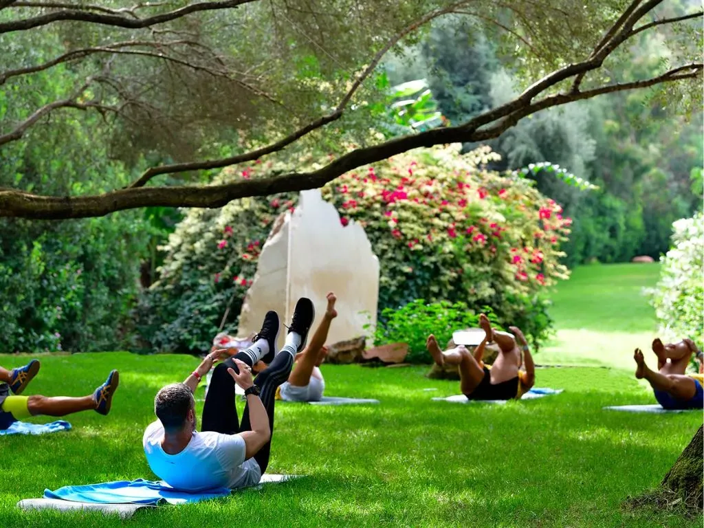 Gruppo di persone fa ginnastica su prato verde all'ombra degli alberi e bouganville fiorita