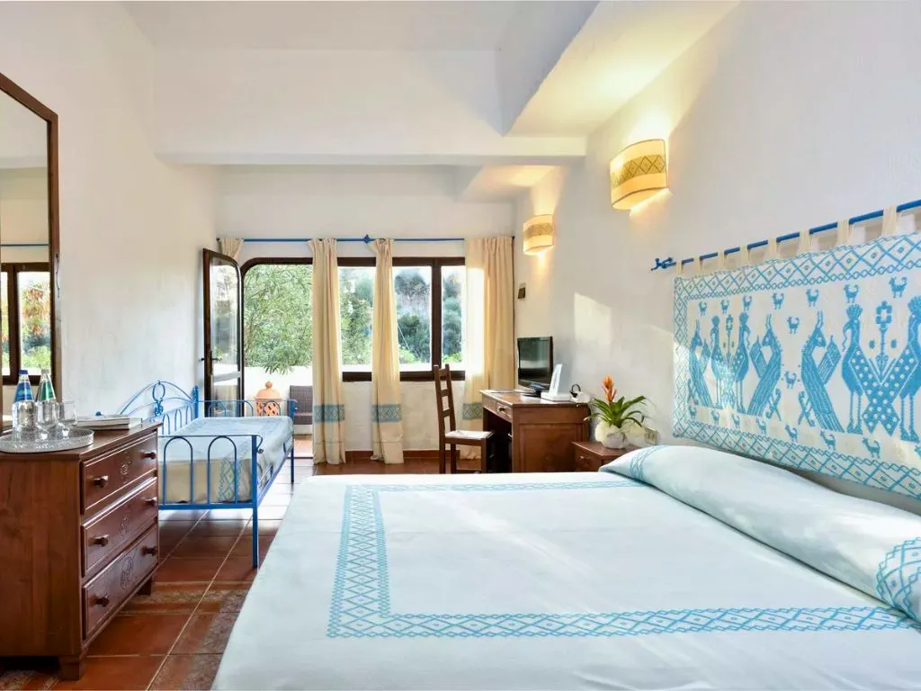 Camera luminosa con letto matrimoniale, arredi in legno e decorazioni tradizionali sarde