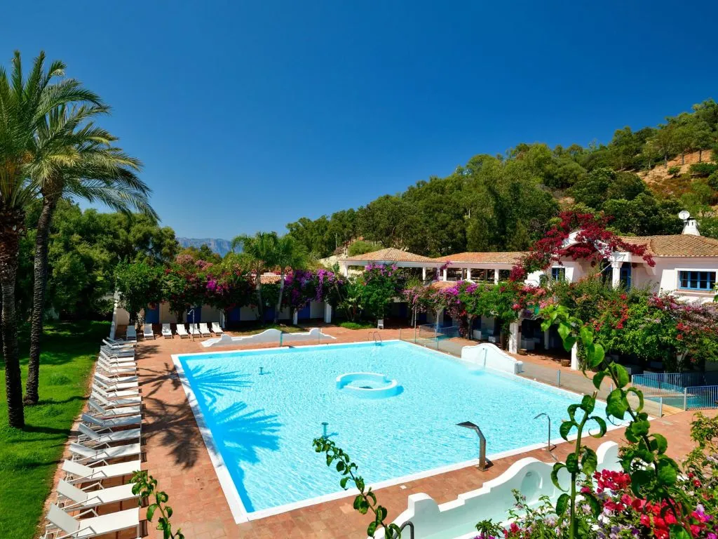 Piscina rettangolare con lettini bianchi, palme e bouganville in fiore