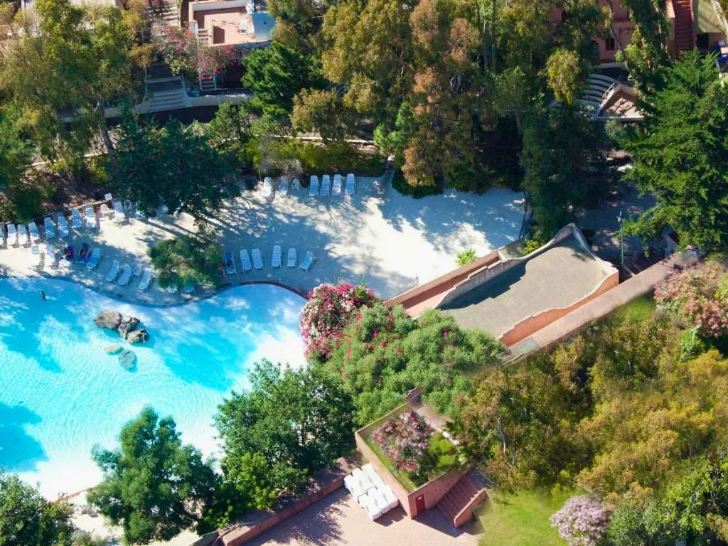 Veduta aerea della piscina con lettini bianchi circondata dalla vegetazione