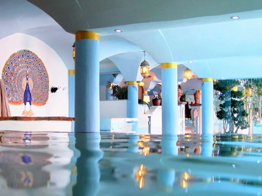 Piscina interna con colonne azzurre e affresco di un pavone sulla parete