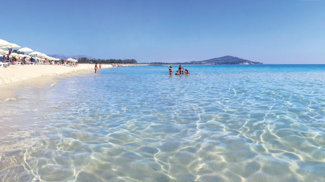 Spiaggia con ombrelloni bianchi, mare cristallino e bagnanti in lontananza