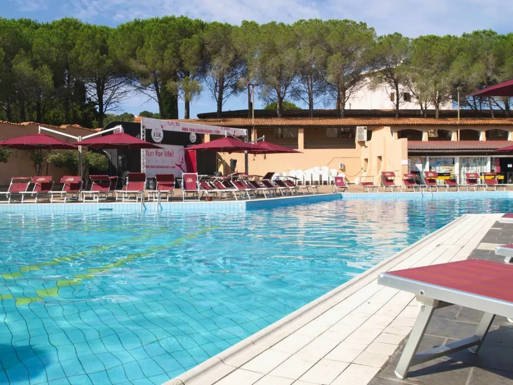 Piscina con lettini rossi, ombrelloni e pini circostanti