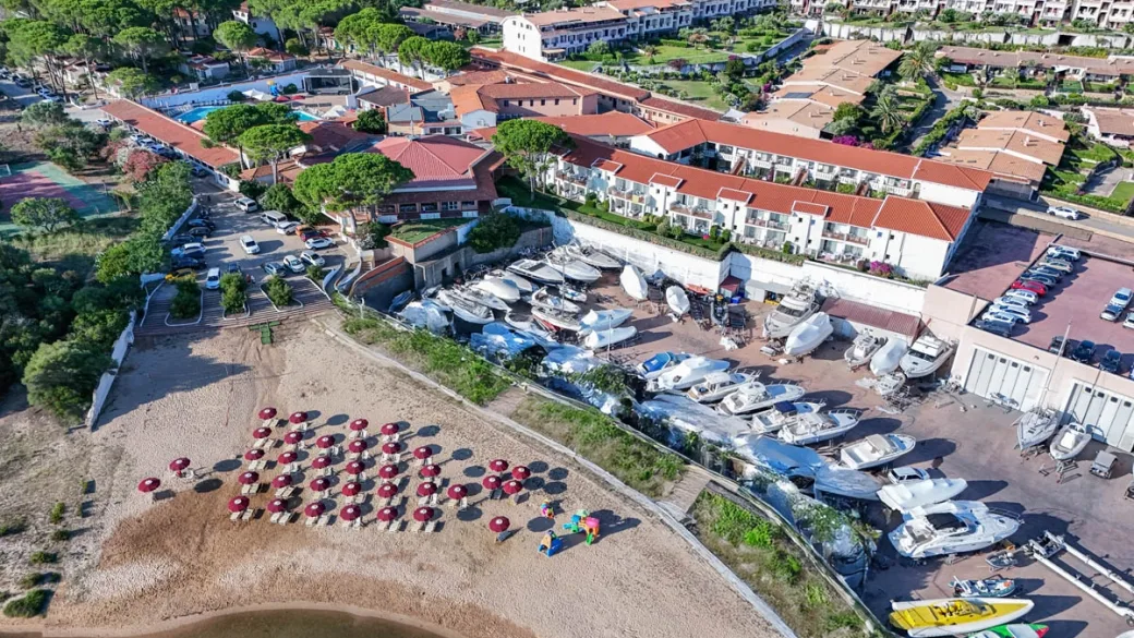 Veduta aerea del resort con rimessa barche e spiaggia con ombrelloni rossi