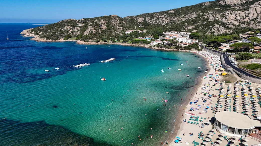 Veduta aerea della spiaggia con mare turchese, ombrelloni e colline circostanti