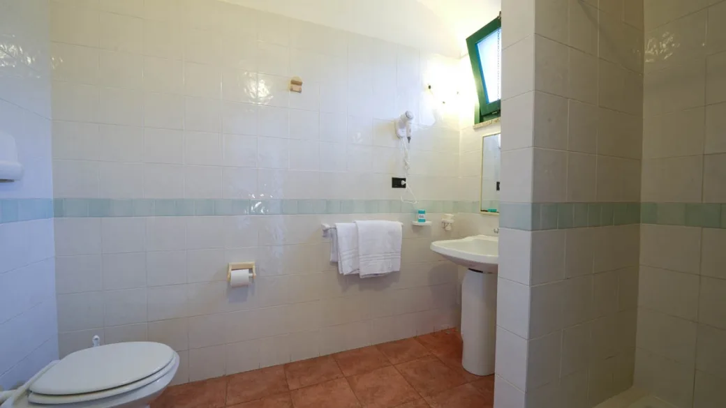 Bagno con piastrelle bianche, lavabo e servizi essenziali