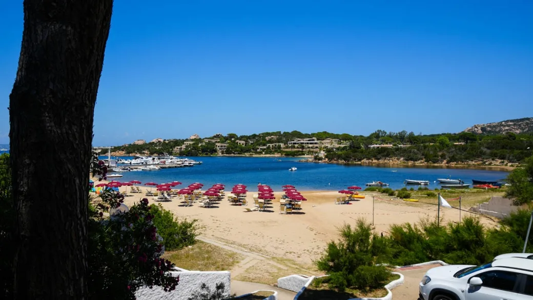 Spiaggia con ombrelloni rossi e porticciolo vista dal resort