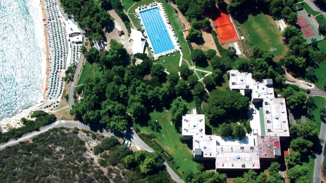 Veduta aerea del complesso con grande piscina, campi da tennis e spiaggia con ombrelloni sul mare