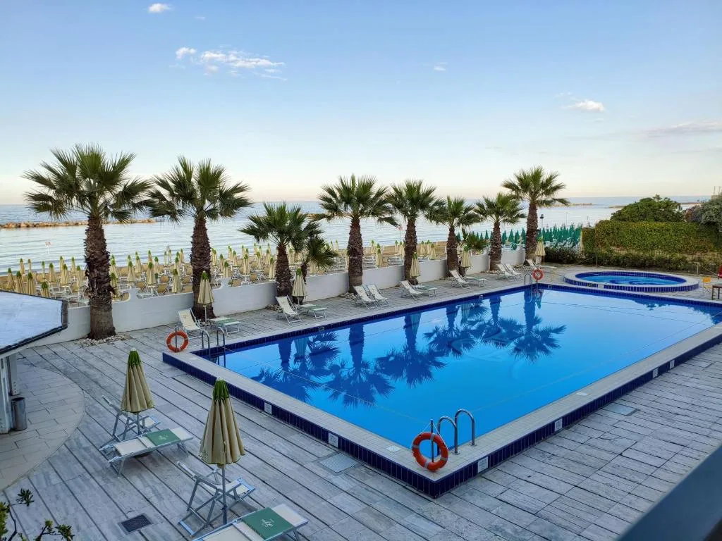 Piscina rettangolare con palme e lettini, vista sul mare al tramonto