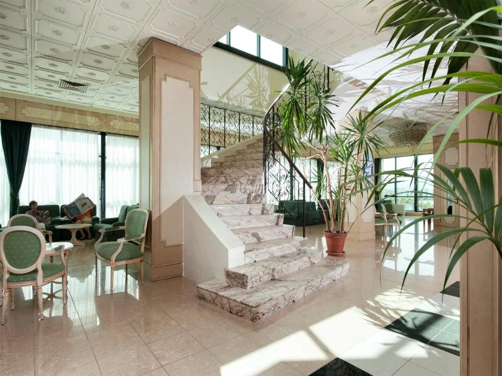Hall dell'hotel con scala in marmo, poltrone verdi e soffitto decorato