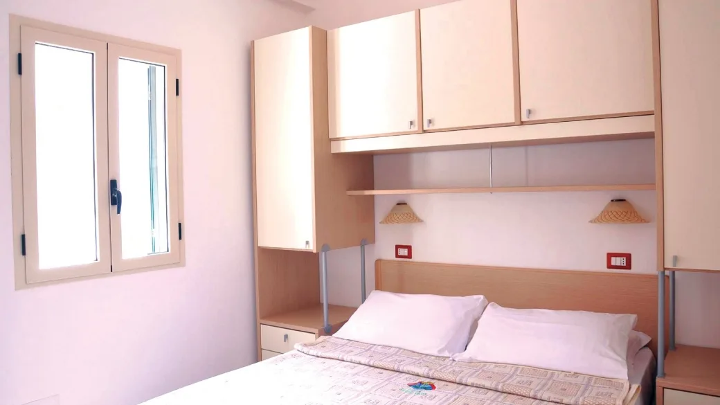 Camera da letto matrimoniale con armadi in legno chiaro, finestra e lampade da lettura