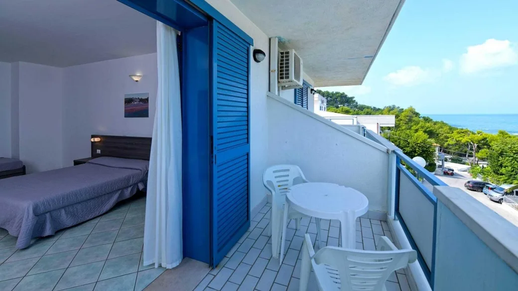 Camera con letto e balcone arredato con tavolino e vista mare
