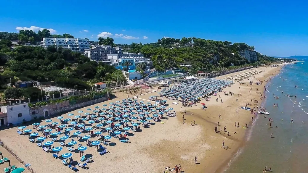 Veduta aerea della spiaggia con file di ombrelloni azzurri e struttura sulla collina