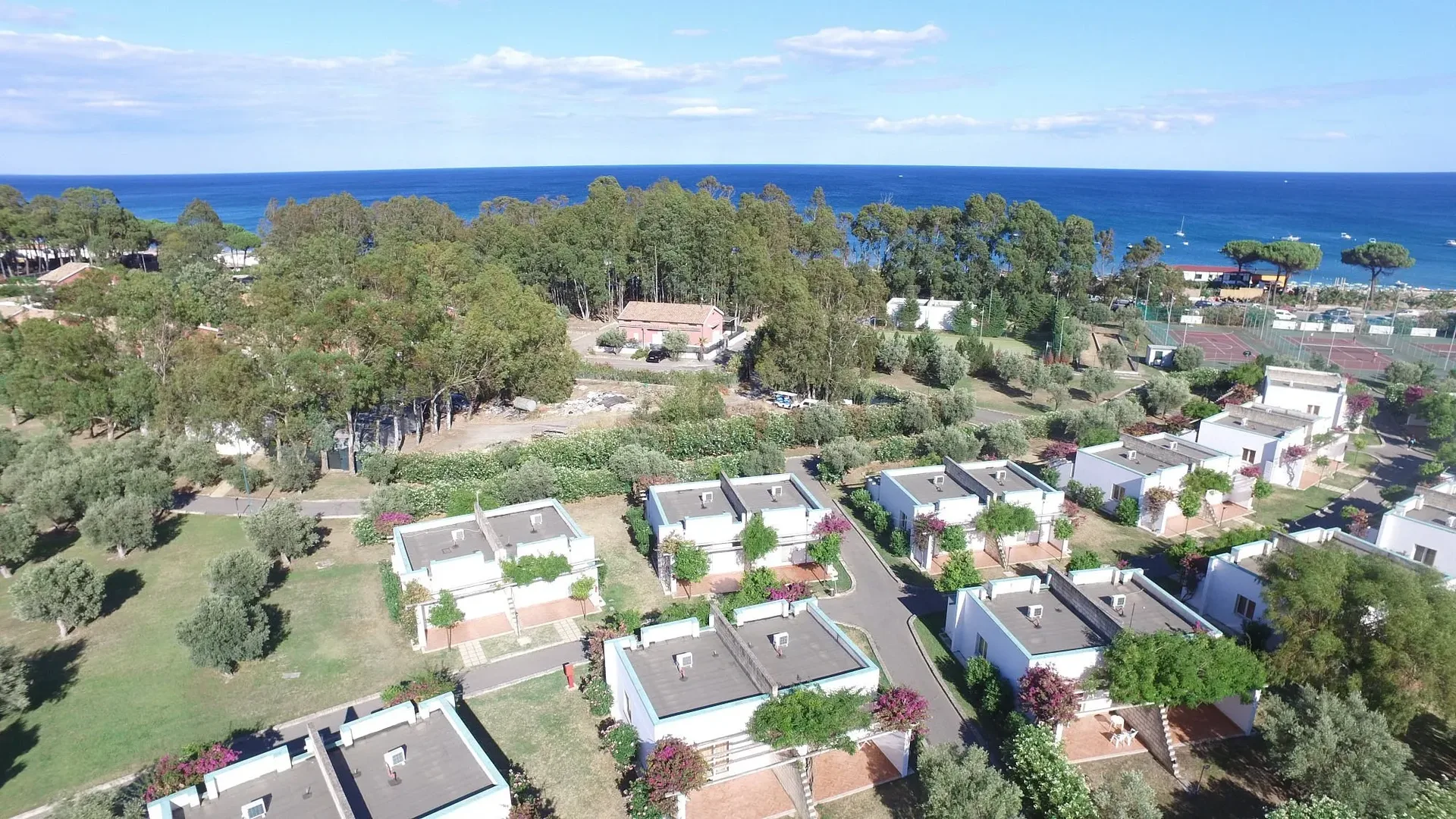Vista aerea delle villette bianche del resort immerse nel verde vicino al mare