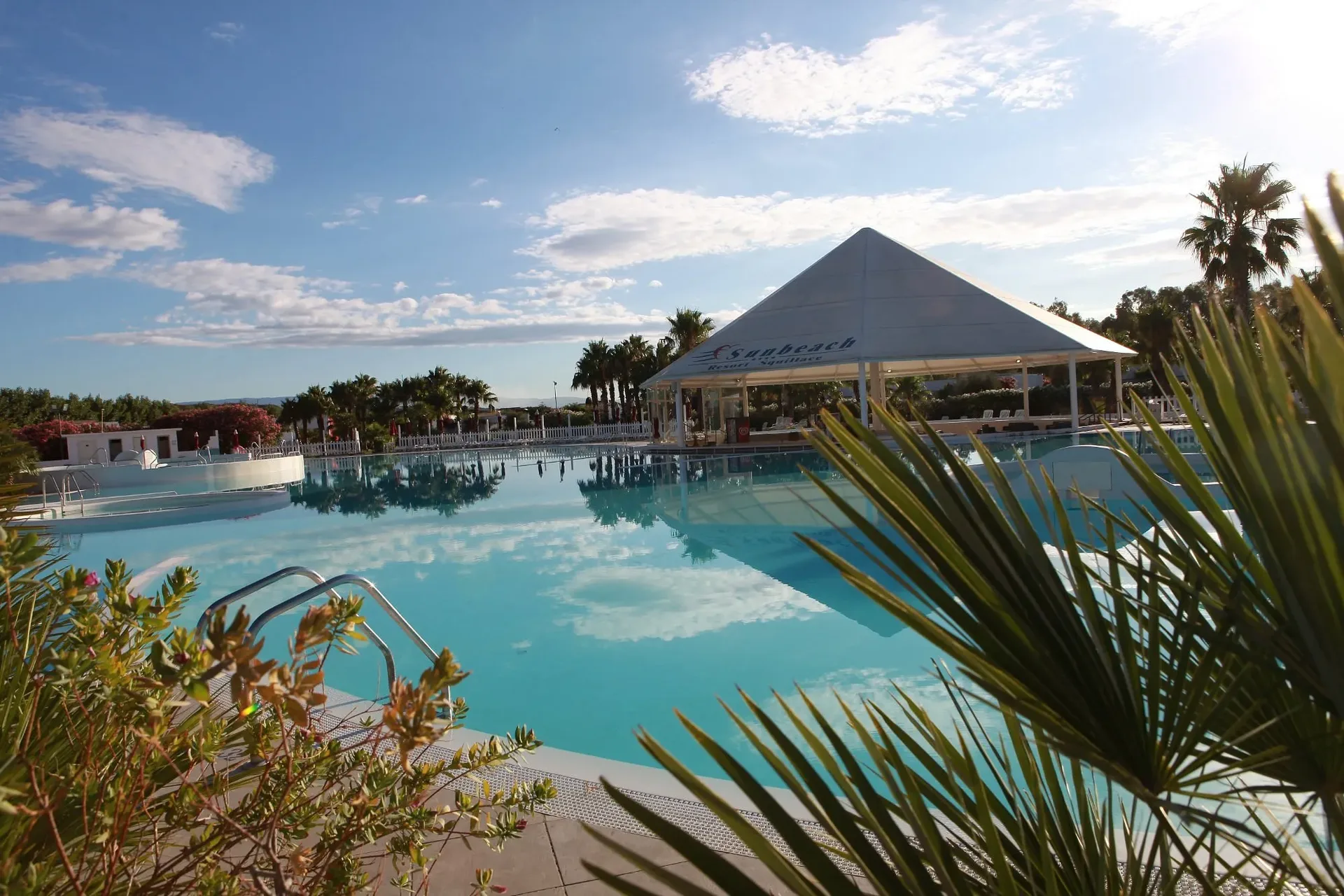 Piscina del resort con gazebo a piramide e palme riflesse sull'acqua