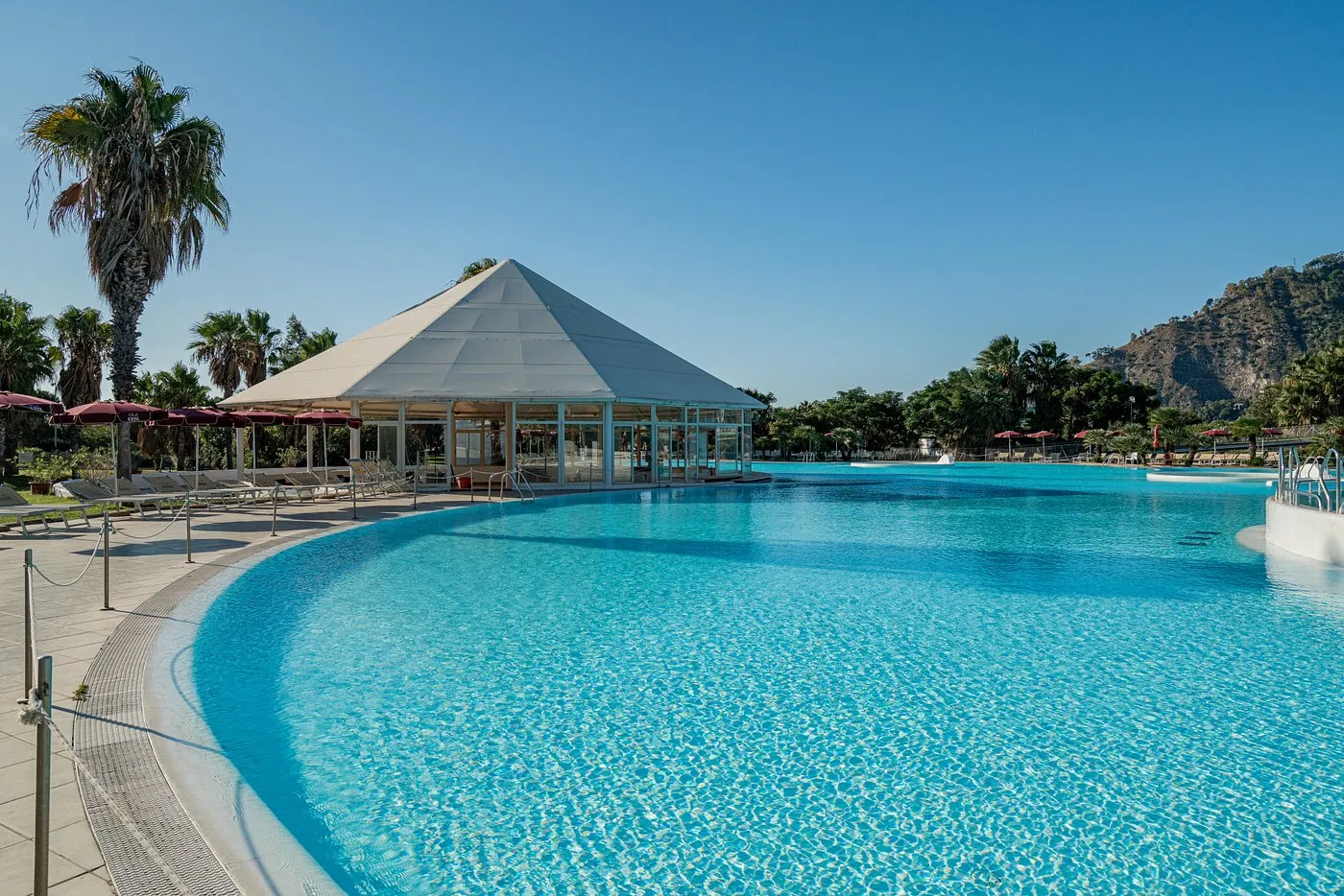 Piscina con gazebo bianco a piramide circondata da palme e lettini