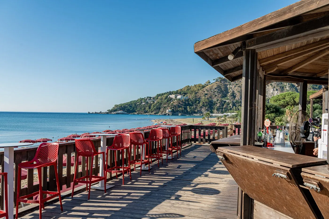 Bar in legno sulla spiaggia con sgabelli rossi vista mare