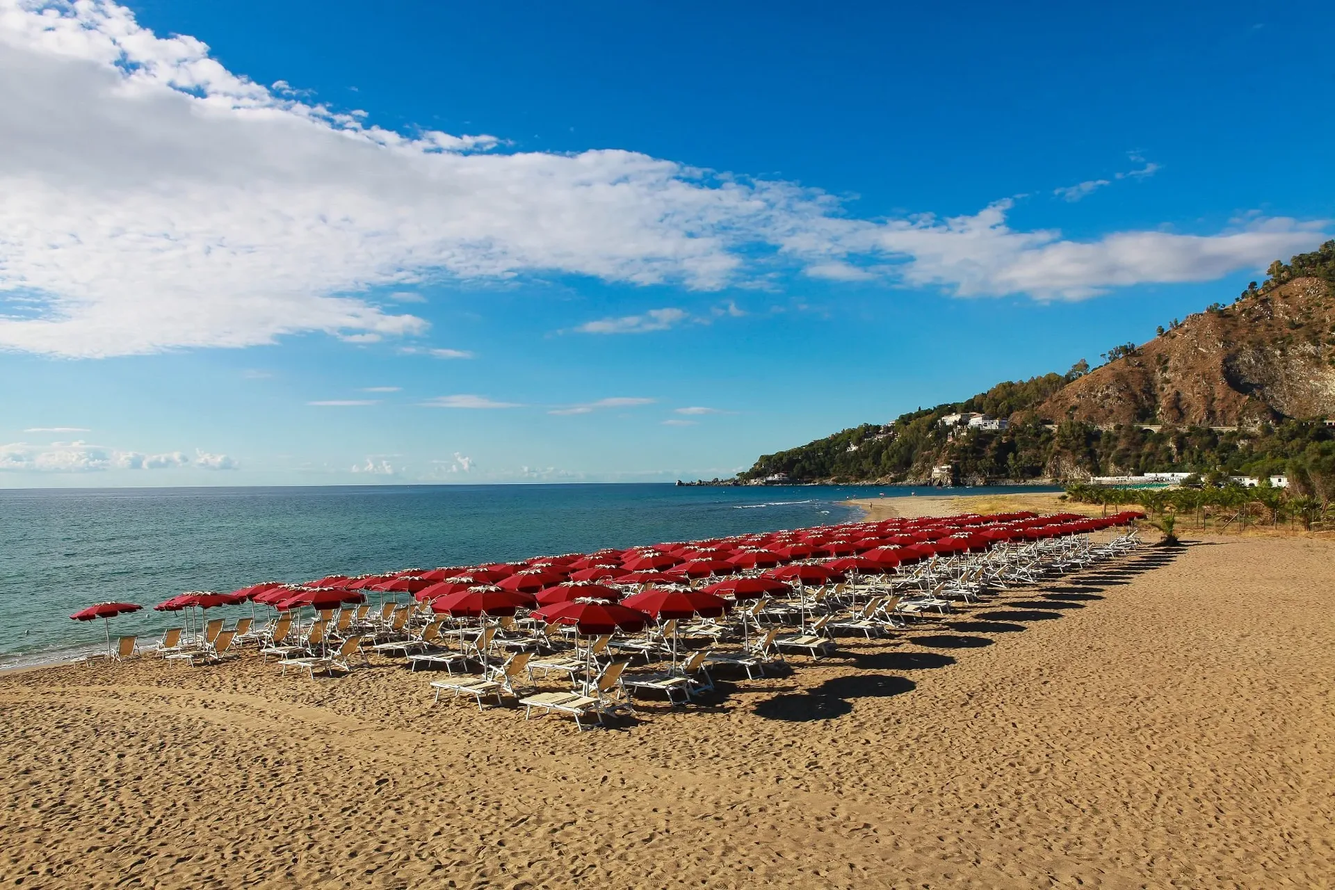 Spiaggia con ordinate file di lettini e ombrelloni rossi affacciati sul mare