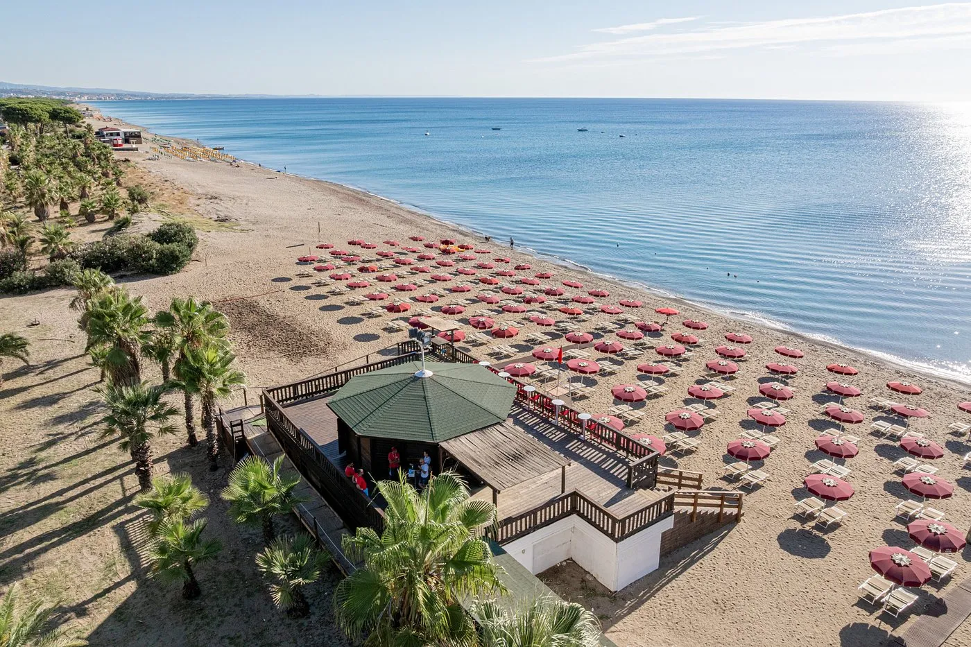 Spiaggia sabbiosa con ombrelloni bordeaux, chiosco in legno e mare sullo sfondo