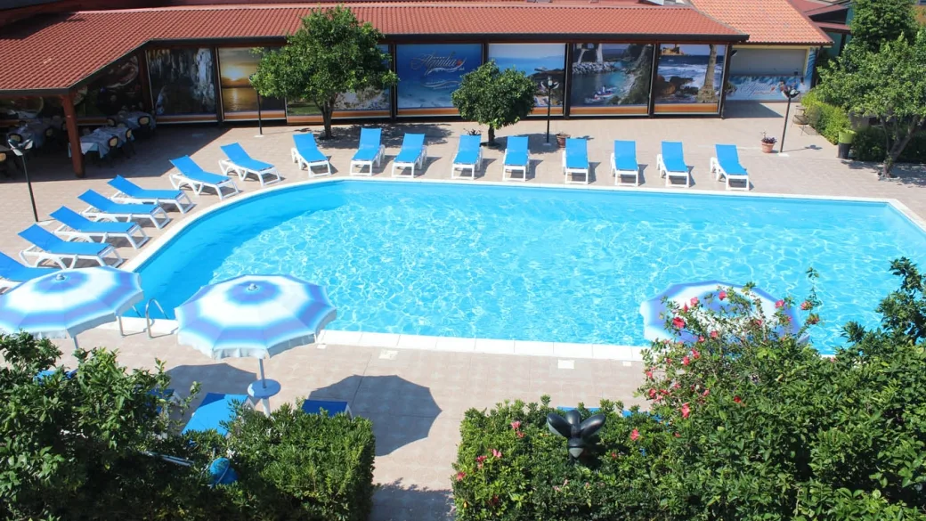 Piscina con lettini blu, ombrelloni e edificio con vetrate decorate