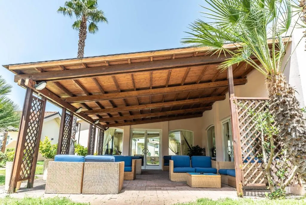 Area lounge esterna con divani in rattan e cuscini blu sotto pergolato in legno