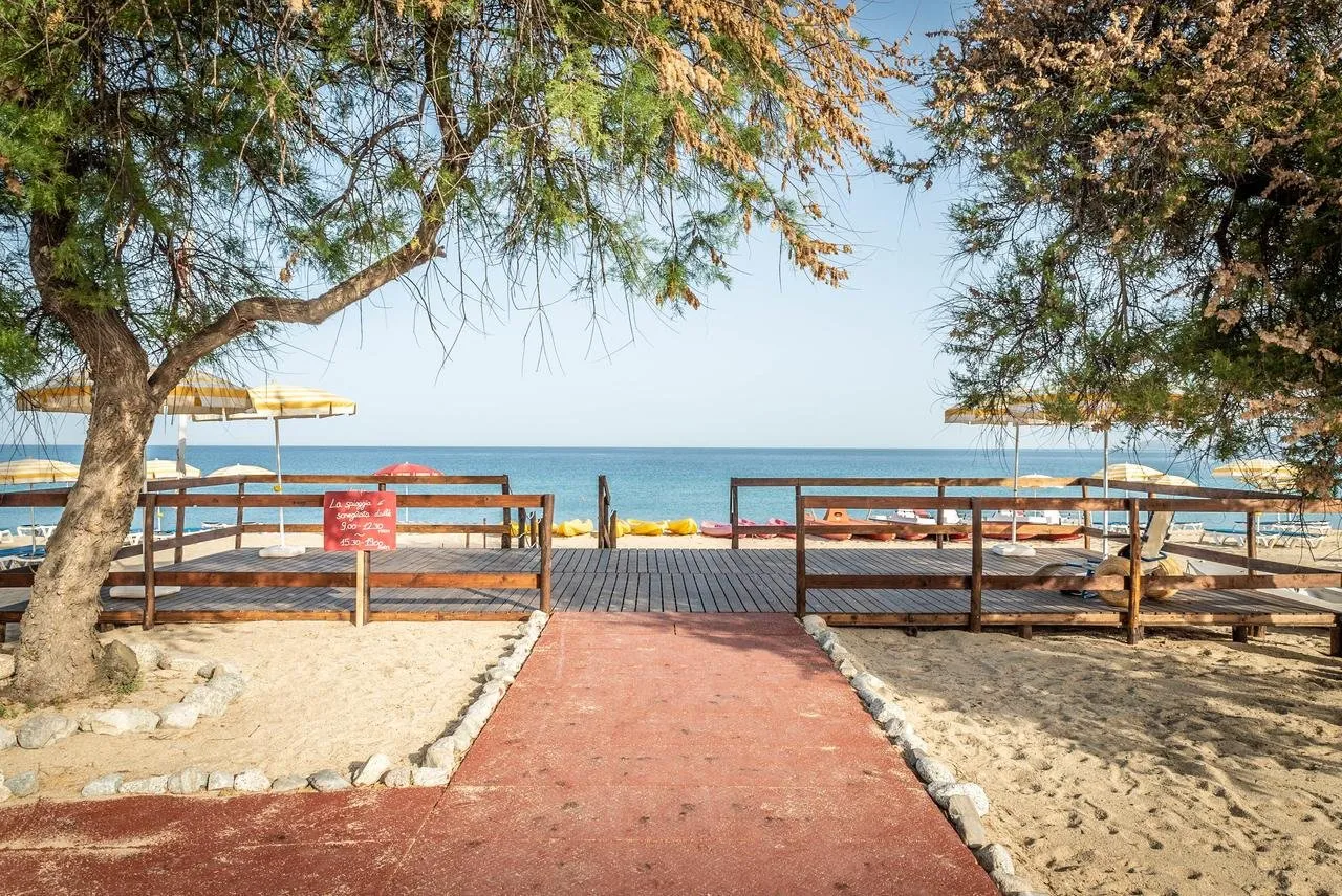 Passaggio in legno verso la spiaggia con ombrelloni gialli e mare sullo sfondo