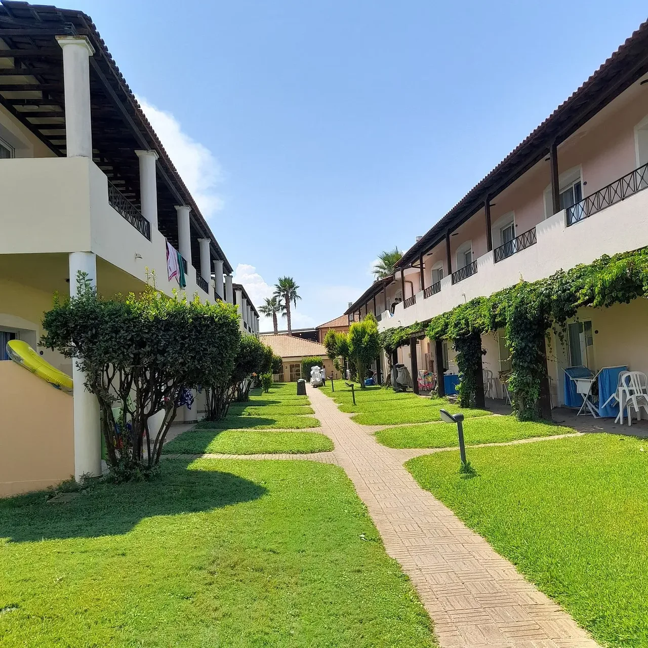 Vialetto tra gli edifici del resort con prato verde e piante rampicanti