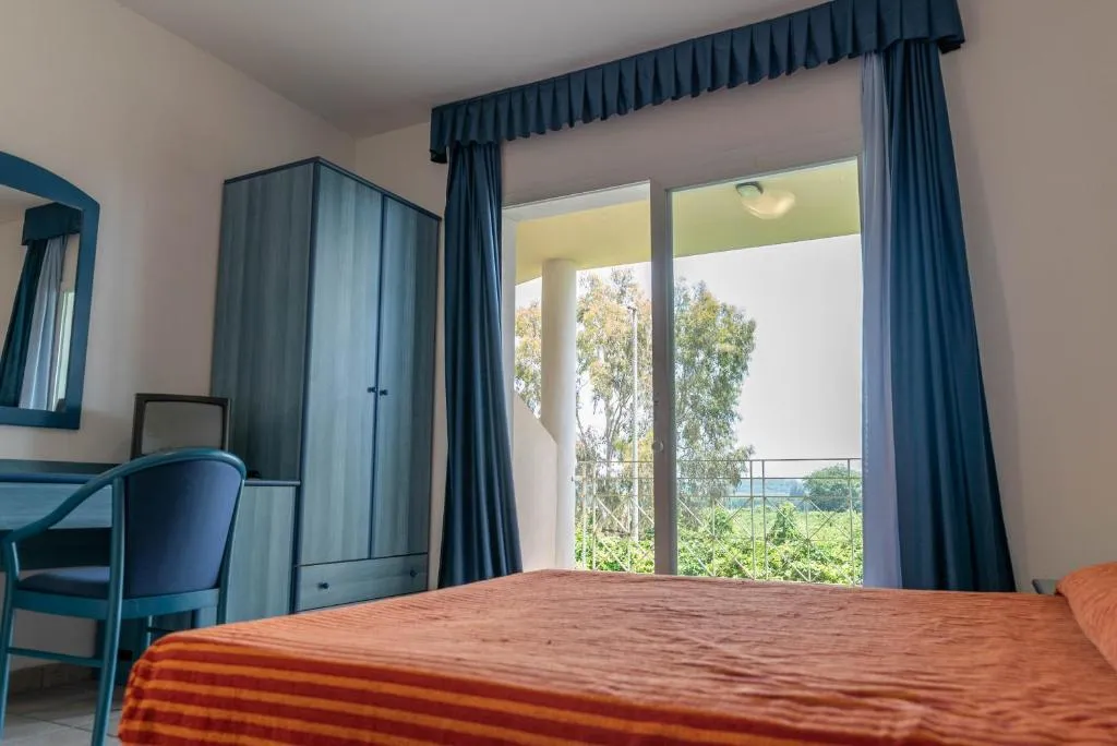 Camera con letto matrimoniale, copriletto arancione e vista sul verde dal balcone